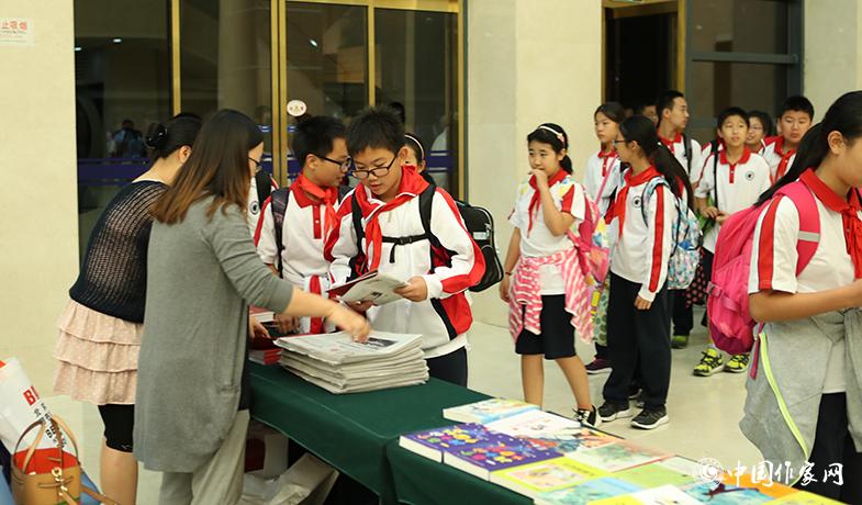 參加頒獎(jiǎng)典禮的學(xué)生排隊(duì)入場(chǎng)，工作人員為他們分發(fā)當(dāng)天的《文藝報(bào)》兒獎(jiǎng)特刊